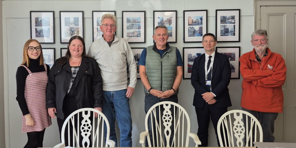 6 trustees stand in front of framed photos from the office exhibition