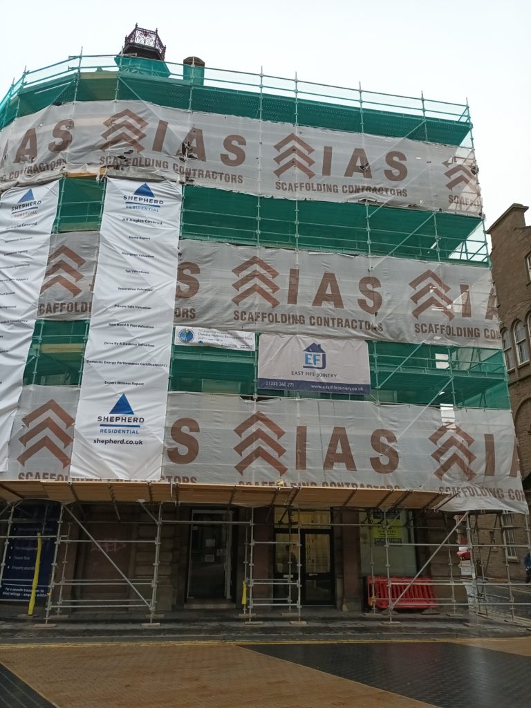 A large corner building covered by scaffolding and banners