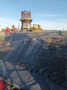 A slate roof with some slates removed and some in the process of being replaced