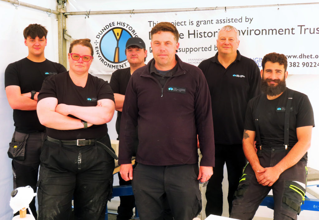 Six people dressed in black with HES logo tops stand facing the camera inside a marquee