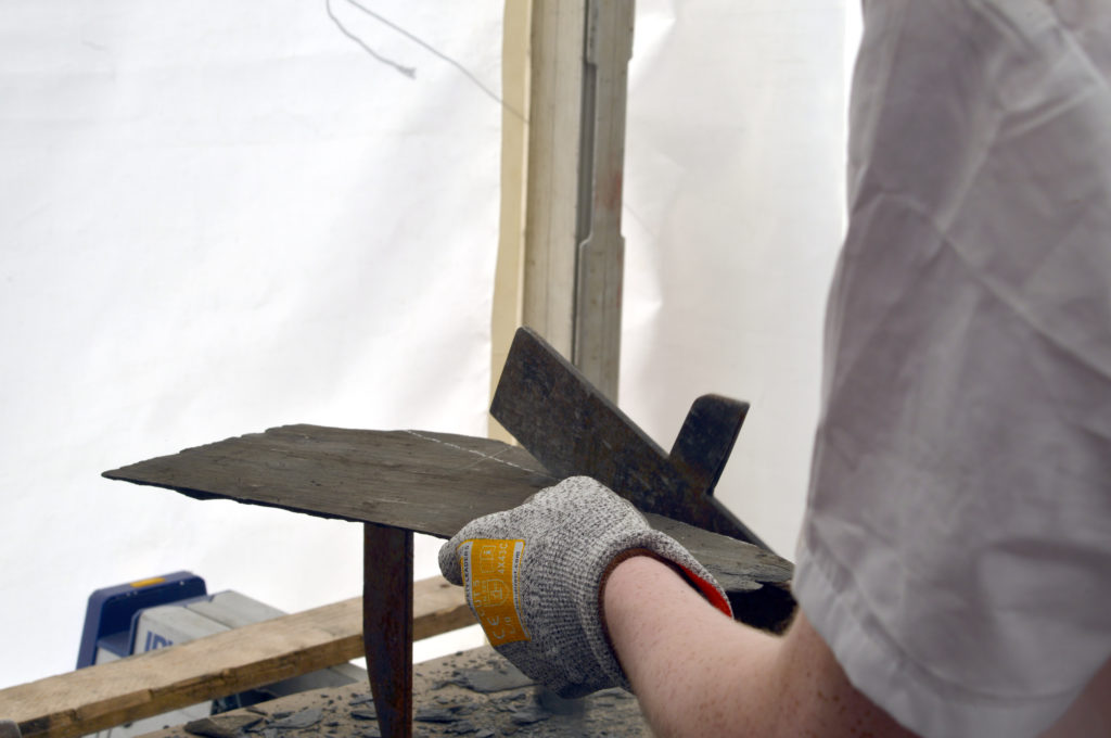 A hand wearing gloves works on a roof slate