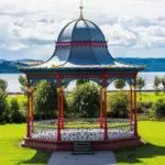 Blue and red historic band stand with grass, trees and blue sky with clouds in the background